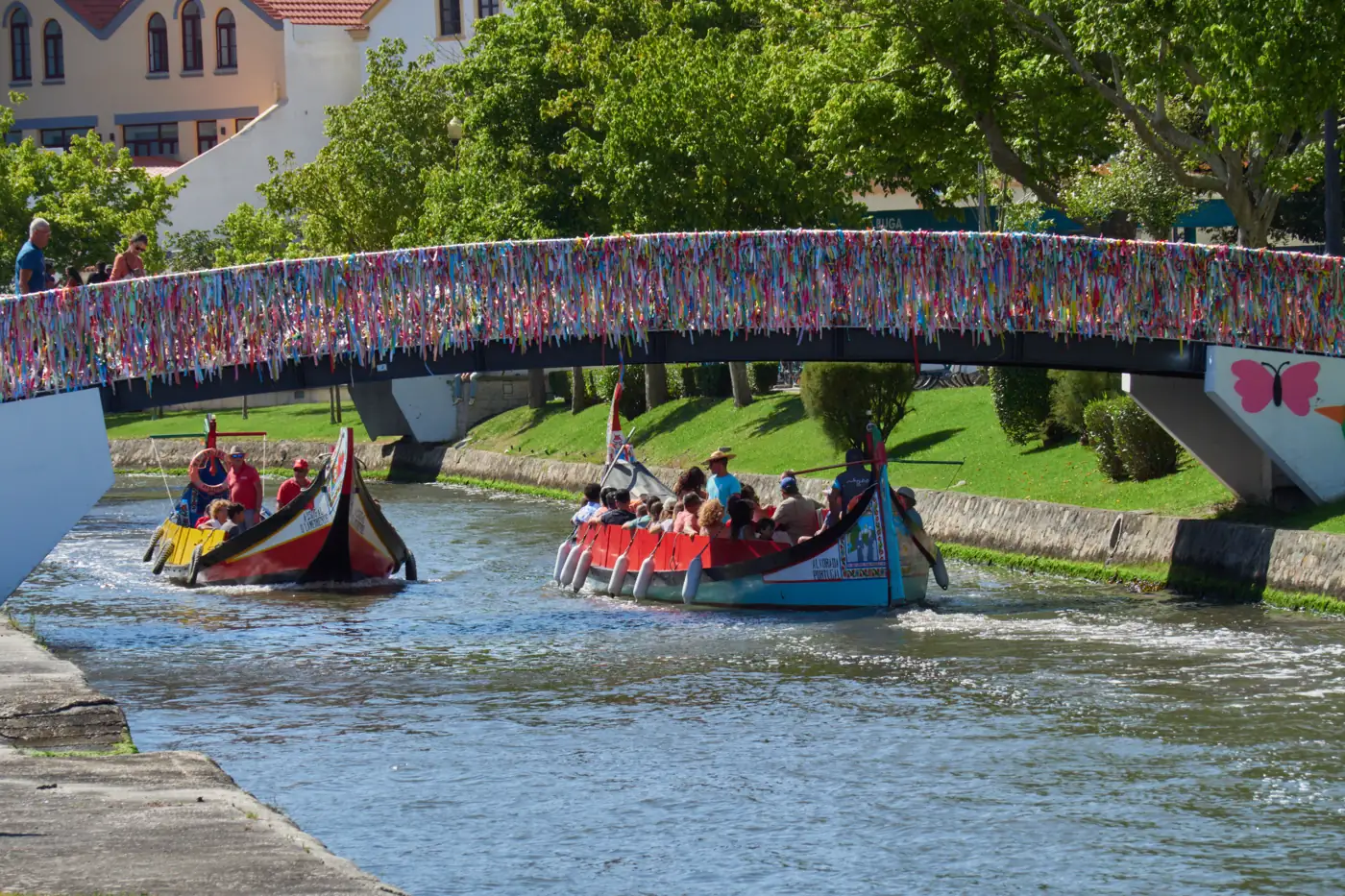 Moliceiros num canal de Aveiro, junto a uma ponte com fitas coloridas.